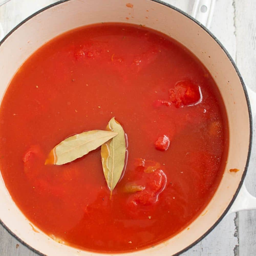 Canned tomatoes in a white Dutch oven with 2 bay leaves.