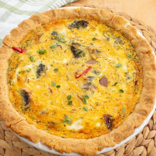 Roasted vegetable quiche in a white pie plate on a bamboo mat.