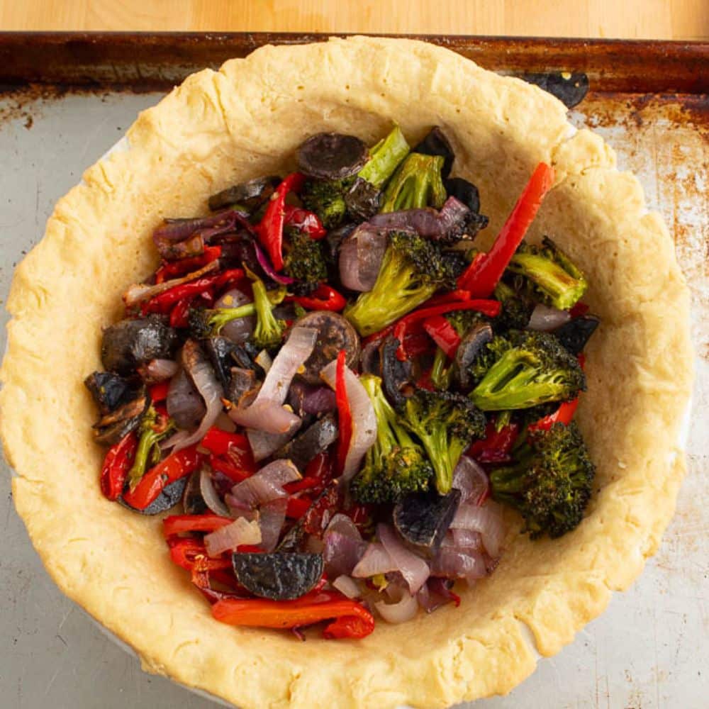 Roasted vegetables in a par baked pie shell on a sheet pan.