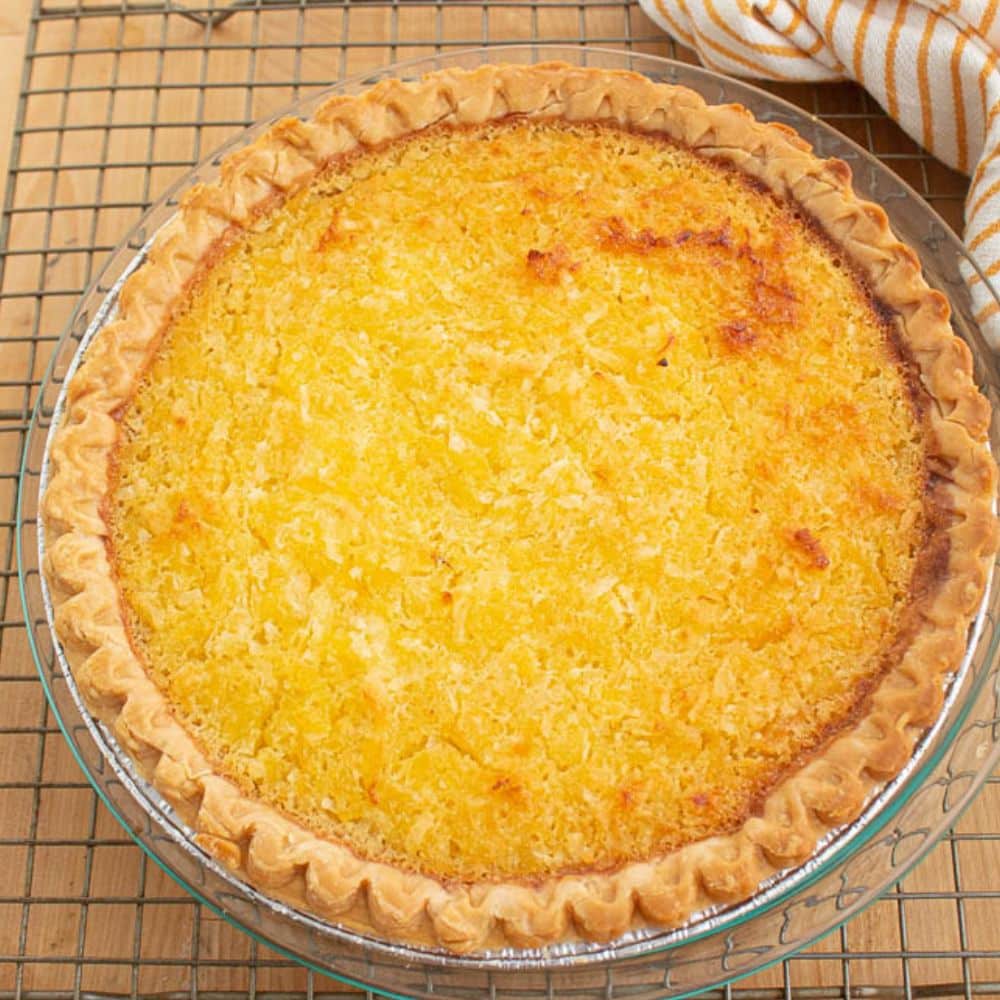 Cooked pineapple coconut pie in a clear pie plate on a wire bakers rack.