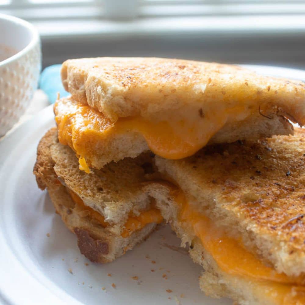 Stack of Grilled Cheese Sandwich Halves on a white paper plate.