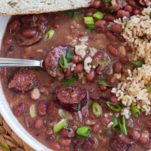 bowlful of crockpot cajun red beans and rice with chopped green onions and parsly on top in a white bowl.