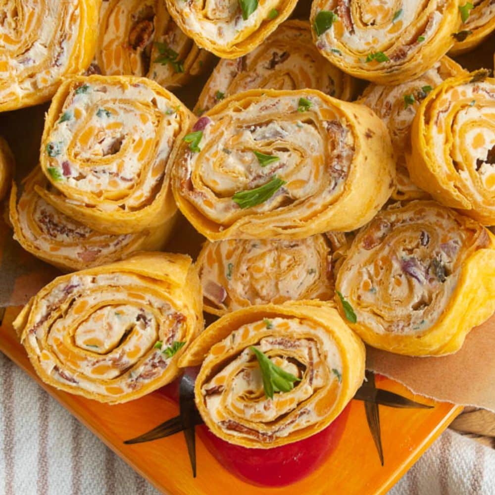 Orange plateful of bacon cheddar ranch tortilla pinwheels roll ups served with salsa.