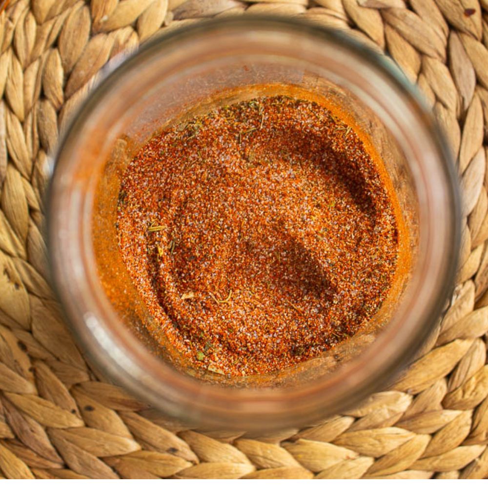 Cajun seasoning blend in a mason jar on a tan bamboo mat.