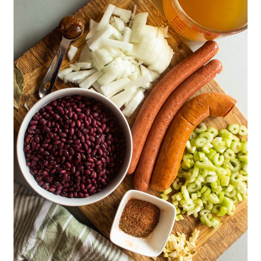 Red Beans and Sausage ingredients on a wood cutting board with a freen and white towel on the side.