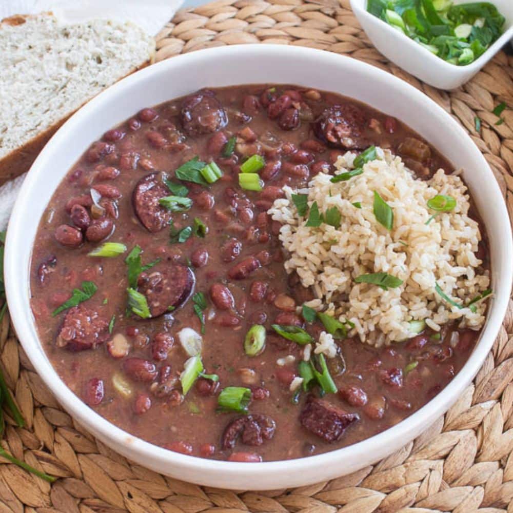 bowlful of crockpot cajun red beans and rice with chopped green onions and parsly on top in a white bowl on a bamboo platemat.